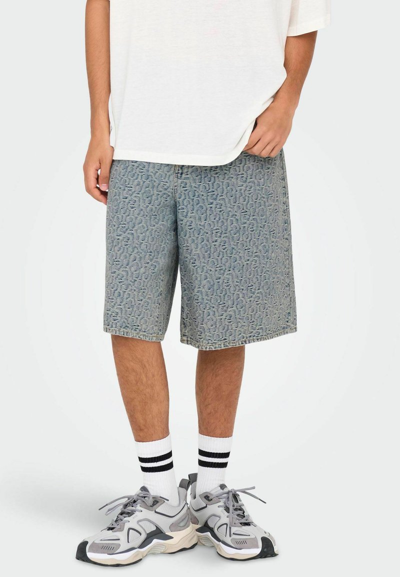 Shorts de mezclilla azul claro con un patrón texturizado, corte clásico y bolsillos laterales, combinados con una camiseta blanca y zapatillas deportivas grises.