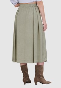 Groene, knielange rok met plooien en een elastische tailleband. G gedragen met bruin suède enkellaarsjes met een iets hogere hak.