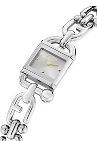 Ceas din metal argintiu cu cadran pătrat și o față gri. Accente aurii pe ace și numele mărcii. Brățară chunky din lanț.