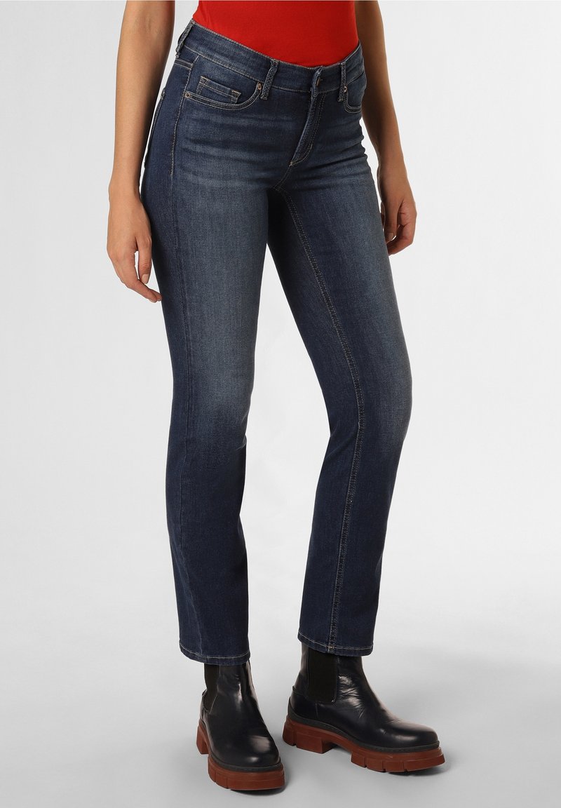 Mörkblå denimjeans med en figursydd design, fem fickor och synlig sömnad. Kombineras med svarta ankelstövlar och en röd topp.