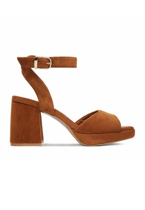 Hnědá semišová sandála s otevřenou špičkou, blokovým podpatkem, páskem kolem kotníku a stříbrnou sponou, zobrazena z boku na bílém pozadí.