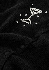 Zwarte stof met een decoratief ontwerp van een drinkglas gemaakt van fonkelende strass-steentjes, met extra verspreide strass-steentjes over het oppervlak.