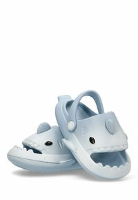 Zuecos de goma de temática de tiburón en azul claro, con aleta dorsal, ojos negros y un diseño de boca abierta con acentos texturizados.