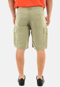 Pantalones cortos cargo en tejido de color verde oliva claro con un acabado texturizado, que incluyen bolsillos laterales y un ajuste relajado. Llevados con zapatillas negras.