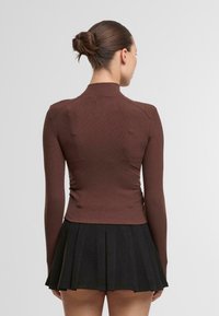 Braunes, geripptes Langarmoberteil mit hohem Kragen, figurbetontem Design und glatter Textur, kombiniert mit einem schwarzen, plissierten Rock.