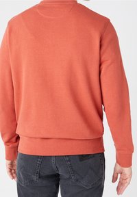 Koraalroze sweatshirt met geribbelde manchetten en zoom, voorzien van een ronde hals. De stof lijkt zacht met een licht geborstelde textuur, gedragen met donkere spijkerbroek.