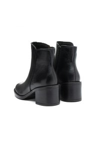 Ein Paar schwarze Lederstiefeletten mit Blockabsätzen und seitlichen Reißverschlüssen, von hinten auf einem weißen Hintergrund gezeigt.
