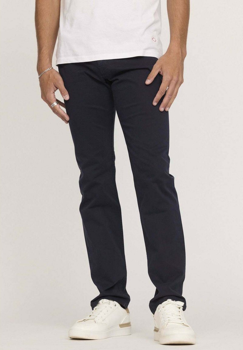 Chinos en coton bleu marine avec une coupe slim, présentant une texture lisse et des poches latérales, associés à des sneakers blanches.