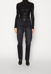 Musta ribbed pusero, jossa on korkea kaulus, yhdistettynä korkeavyötäröisiin, suoriin tummansinisiin farkkuihin, ja asusteena teräväkärkiset mustat nilkkasaappaat.