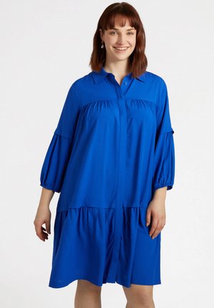 Blaues Hemdblusenkleid mit gepufften Ärmeln, das ein gestuftes Design und eine weiche, glatte Textur aufweist. Der Stoff ist leicht und fließend.