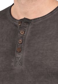 Grå bomulds henley skjorte med rund hals, med en stolpe med fire brune knapper og struktureret stofdetalje nær kraven.