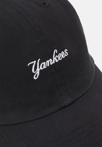 Schwarze Baseballmütze aus strukturiertem Stoff mit weißem, gesticktem "Yankees"-Text auf der Vorderseite. Gewölbter Schirm und verstellbarer Riemen.
