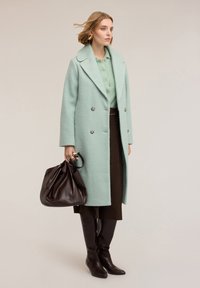 Mintgrön kappa i dubbelradig ull med texturerad yta, kombinerad med brun högmidjad kjol och bruna knähöga läderstövlar.