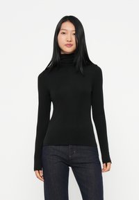 Melnas garās piedurknes turtlenecks, izgatavots no elastīga auduma, pielāgota dizaina, gluda tekstūra, kombinēts ar tumšām džinsu biksēm.