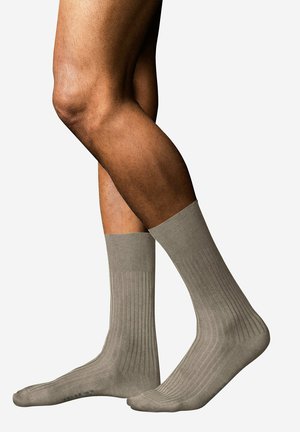 Pair of medium brown ribbed crew socks worn on crossed legs against white background.