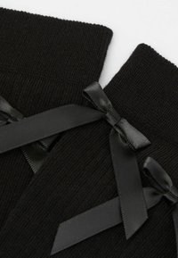 Schwarze Stricksocken mit einem Rippstrick-Muster, die oben mit schwarzen Satinschleifen verziert sind und so einen mehrschichtigen Look für zusätzliche Details schaffen.