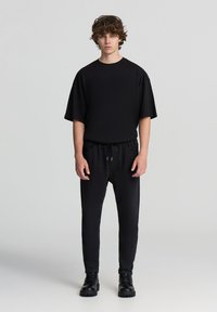 Czarna koszulka z krótkim rękawem, w zestawieniu z czarnymi spodniami na sznurku i czarnymi botkami za kostkę. Gładki design i miękki materiał.