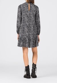 Blommigt mönstrad marinblå klänning med långa ärmar och en nyckelhålsdetalj i ryggen. Utsvängd nederkant och bar med svarta snörkängor.