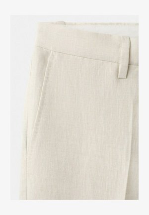 Primer plano de pantalones de lino beige que muestran la cintura, presilla para cinturón y bolsillo lateral con detalles de costuras visibles.