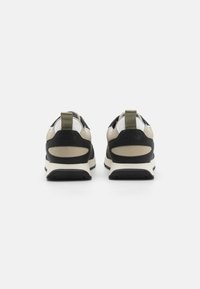 Baskets avec un dessus noir et kaki, présentant un design texturé, des accents blancs et une languette à l'arrière. Semelle en caoutchouc pour une meilleure adhérence.