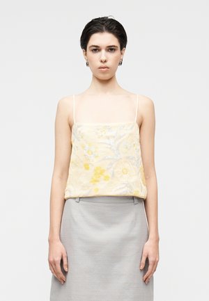 Camisola amarilla bordada con patrones florales y detalles plateados, combinada con una falda gris claro, que presenta una textura suave y tirantes finos.