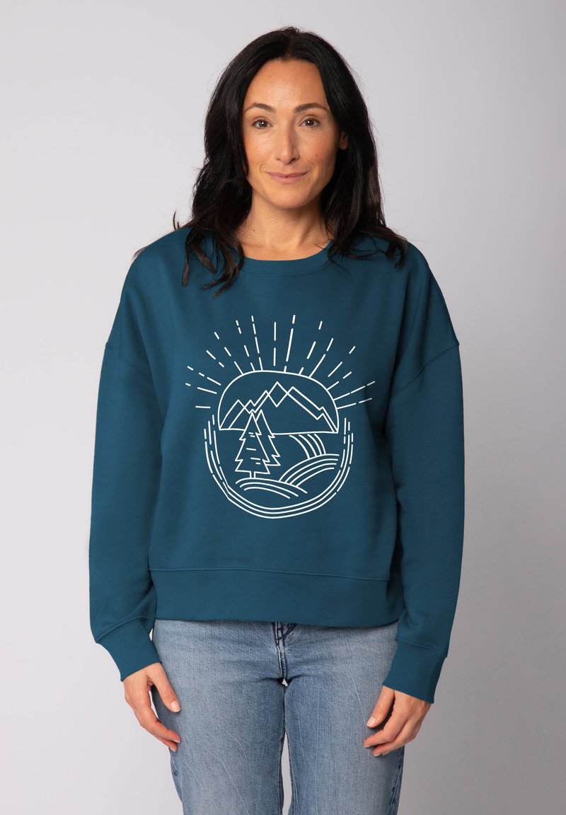 Teal sweatshirt met ronde hals, voorzien van een witte afbeelding van een berg en een boom. Zachte stof met een ontspannen, licht oversized pasvorm.