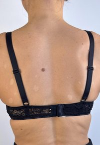 Sostén de encaje negro con tirantes ajustables, un cierre de gancho y ojo, y una banda de encaje texturizada en la parte trasera. Tela suave, diseño minimalista.