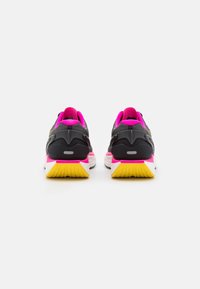 Scarpe da ginnastica nere con interno rosa e suola gialla, caratterizzate da una suola con motivo e dettagli riflettenti sul retro.