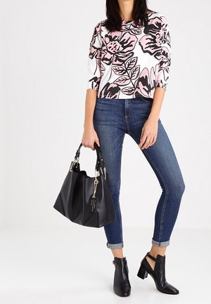 Blommönstrad kortärmad topp med rosa och svarta blommor, i kombination med tighta blåjeans, svarta klackbooties och en svart handväska.