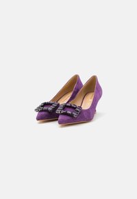 Zapatos de tacón de punta afilada de ante morado con acentos de hebilla de gema negra gruesa, con un tacón bajo de cuña y un forro interno suave.