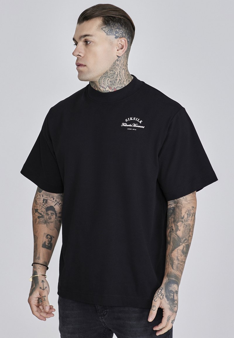 Black cotton oversized t-shirt with short sleeves, featuring a small white logo on the chest and a smooth texture.