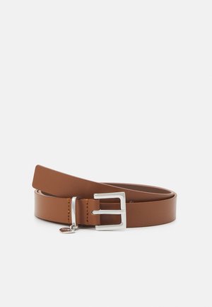 Ceinture en cuir marron enroulée avec une boucle rectangulaire argentée et un petit pendentif rond argenté attaché sur fond blanc.