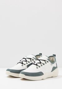 Chaussures de sport blanches avec des accents gris, présentant un design élégant, une surface texturée et des lacets noirs. Bout arrondi et semelle légère.