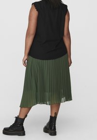 Czarny bezrękawnik z falbaniastymi brzegami; oliwkowa plisowana spódnica; czarne buty na sznurówki z grubą podeszwą i żółtymi detalami.