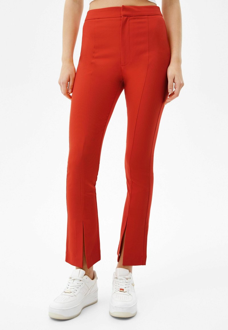 Pantalons rouges ajustés avec une texture lisse, fentes latérales au bas et une taille mi-haute. Assortis avec des baskets blanches.
