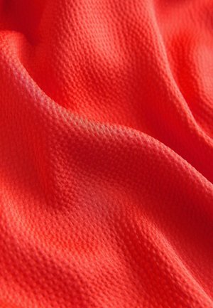 Tessuto rosso brillante con una trama sottile, caratterizzato da morbide pieghe ondulate che mettono in risalto la sua leggerezza e traspirabilità.