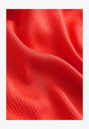 Jasnoczerwona, teksturowana tkanina z subtelnym wzorem, prezentująca miękkie, falujące fałdy podkreślające jej lekkość i przewiewność.