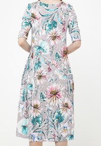 Takakuvatutu dressi, joka ulottuu polveen ja jossa on 3/4-hihaset, esittelee värikästä kukkakuosia vaaleanharmaalla taustalla.