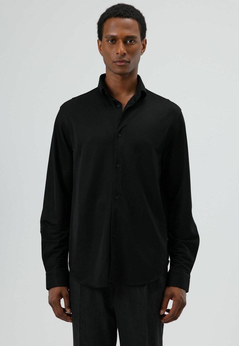 Chemise noire à manches longues avec boutons, col pointu et texture lisse. Présente un ourlet arrondi et des boutons noirs simples.
