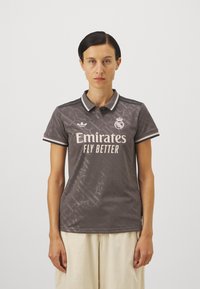 Siva polo majica s diskretnim uzorkom, ovratnikom i kratkim rukavima. Sadrži logo i natpis "Emirates Fly Better" u svijetlim bojama.