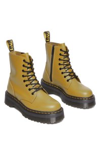 Bottines en cuir jaune avec lacets noirs, fermeture éclair sur le côté, et semelle noire épaisse avec une couture orange. Onglet de traction jaune à l'arrière.