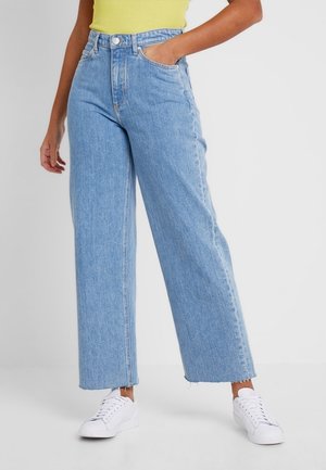 Lyseblå vidde jeans i denim med høj talje, frontlommer og frynset kant, parret med hvide sneakers.