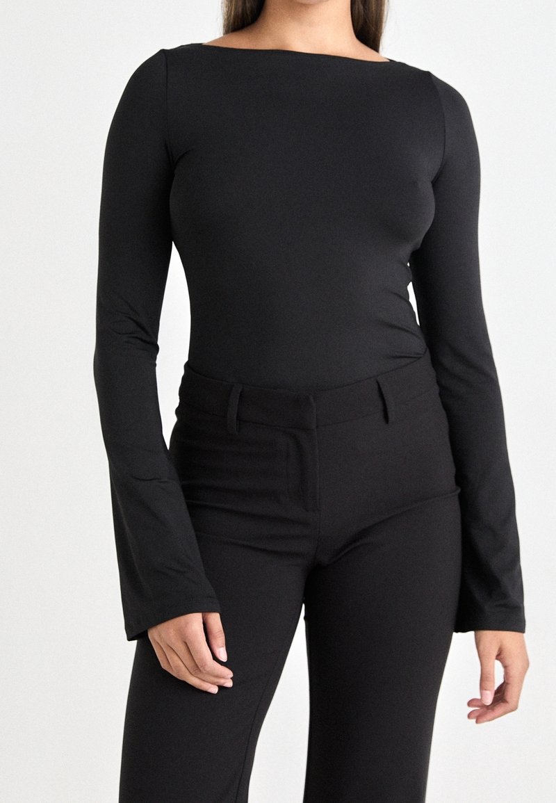 Schwarzer Longsleeve-Bodysuit mit Bootsausschnitt und figurbetontem Design. Kombiniert mit hoch geschnittenen schwarzen Hosen. Glatter, dehnbarer Stoff.