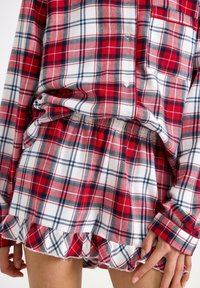 Chemise à carreaux rouge et blanc avec des accents bleu marine, dotée d'une poche et de détails en boutons, associée à un short à volants assorti. Tissu doux.