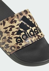 Tongs Adidas avec une sangle en imprimé léopard marron et beige, semelle noire à finition mate et logo en relief sur la sangle. Semelle intérieure texturée.