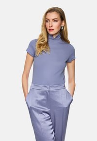 Lila kurzärmliger Rollkragenpullover aus glattem, dehnbarem Stoff, kombiniert mit helllila Satin-Hosen mit Seitentaschen und Falten.