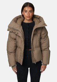 Puchowa kurtka w jasnobrązowym kolorze, z dużym, usztywnionym kapturem, ściągaczami u mankietów, zamek błyskawiczny oraz pudełkowym krojem. Miękka faktura, pikowany wzór.