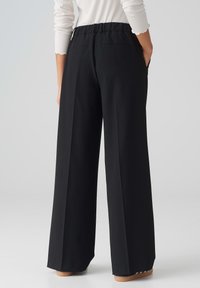 Black wide-leg trousers with a relaxed fit, elastic waistband, and two back pockets. Smooth texture and lightweight fabric.