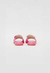 Pink flat sandals with an open back, soft strap design, and a small block heel. Smooth texture with a minimalistic aesthetic.