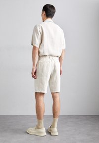 Camicetta in lino beige chiaro a maniche corte e pantaloni corti coordinati con cintura elastica. Tessuto morbido e vestibilità comoda. Scarpe slip-on beige chiaro.